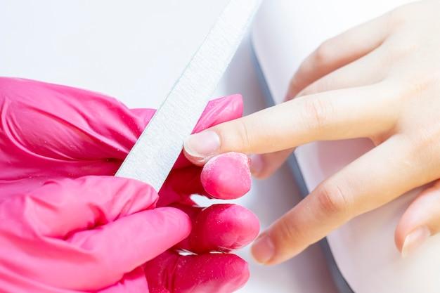 Manicurist filing client's nails with a nail file during a manicure session.