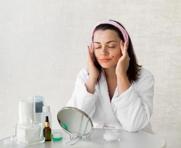 Woman in white robe applying skincare products