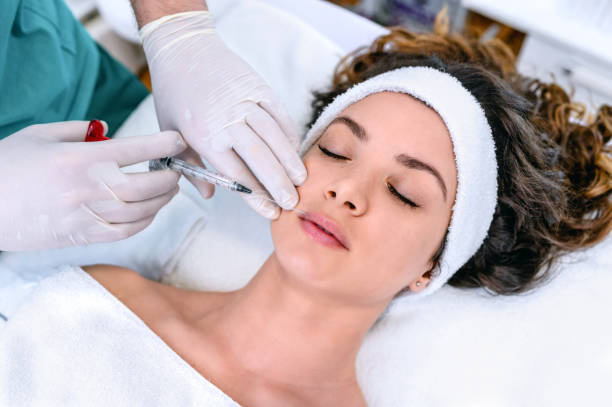 This image shows a woman receiving a cosmetic procedure, likely an injection, from a healthcare professional wearing gloves.