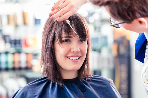 Stylist applying hair treatment to smiling woman in salon